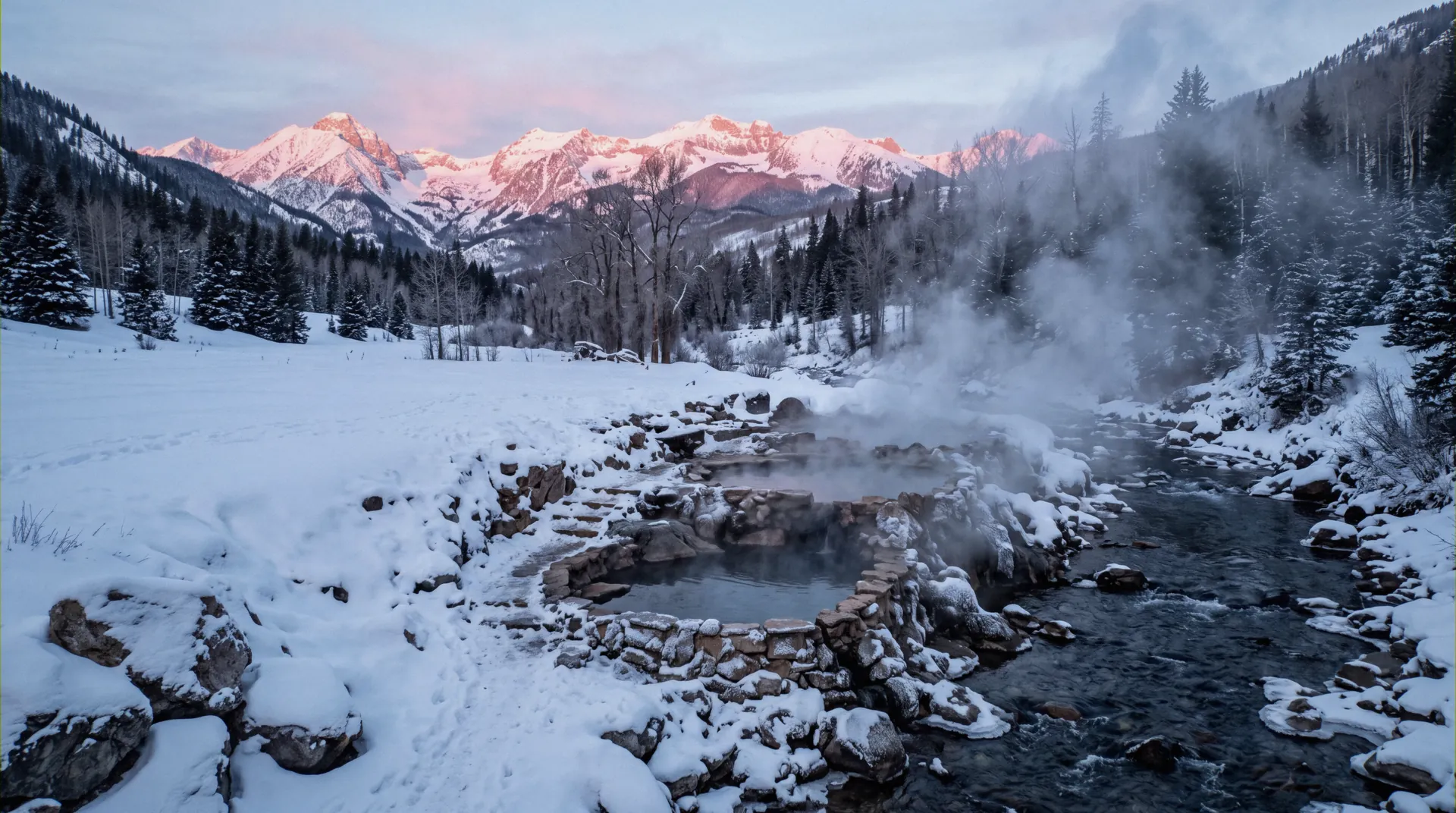 Steaming hot spring pools on a snowy riverbank below Colorado fourteeners at sunrise